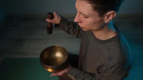 Close-up of a man playing a Tibetan singing bowl with a wooden mallet, focusing Video stock 304032867