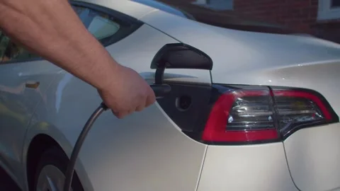 Close up of man plugging charger into white electric car at home Stock Footage 335953178