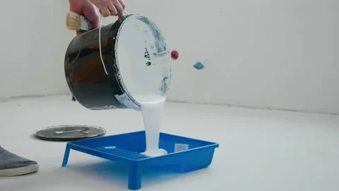 Close-up of a man pouring white paint from a bucket into a construction tray. 库存影片 148166892