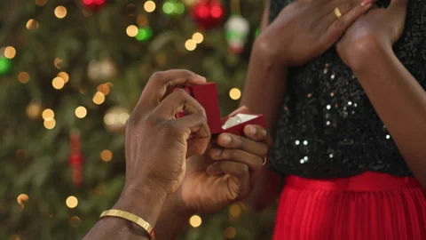 Close-up of a man presenting an open ring box to a woman in front of a Christmas Stock Footage 341022035