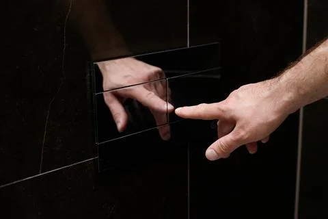 Close-up of a man pressing the chrome button to flush the toilet in the bathr Foto stock