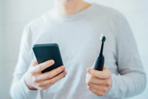 Close up man puts settings of his electronic toothbrush with mobile phone app Stock Photos