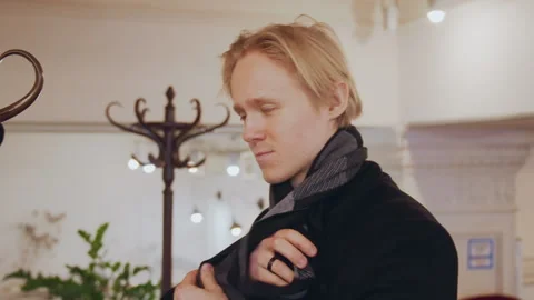 Close up of man putting on and adjusting gray scarf in soft indoor lighting with Stock Footage 344866305