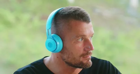 Close-up of man putting blue wireless headphones and listening music outdoor. Stock Footage 246774352