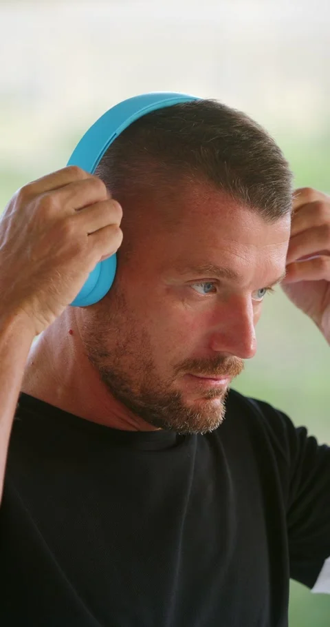 Close-up of man putting blue wireless headphones and listening music outdoor. Stock Footage 246777895
