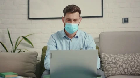 Close up man remove medical protective mask working on wireless laptop at home 動画素材 132540127