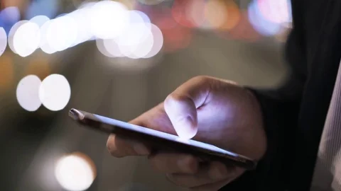 Close up of man s hand swiping across a cell phone screen near a night road Stock Footage 80786636
