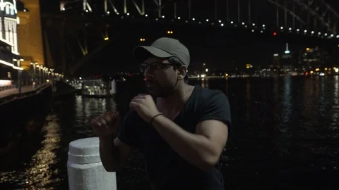 Close Up Man Shadow Boxing on Wharf in Front of Sydney Harbour Bridge at Night Stock Footage 107901339