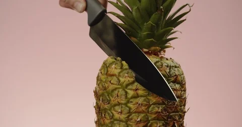 Close-up of man with sharp knife cuts off slice from whole pineapple Stock Footage 125025573