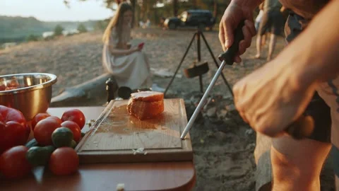 Close-up of a man sharpening a knife for cooking at a picnic with friends on the 库存影片 220491719