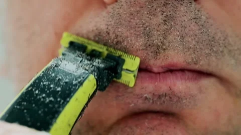 Close-up of man shaving upper lip area with electric trimmer slow motion de.. Vidéo 335134206