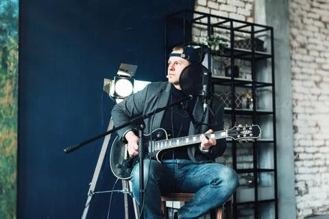 Close up of a man singer sitting on a stool in a headphones with a guitar rec Stock Photos