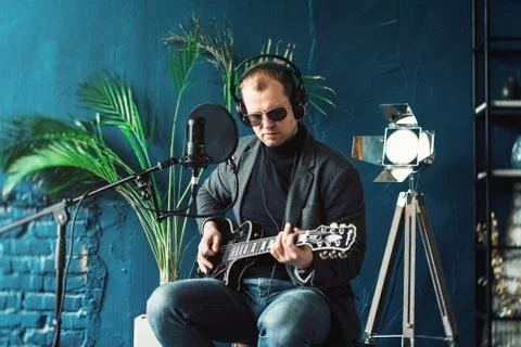 Close up of a man singer sitting on a stool in a headphones with a guitar rec Stock Photos