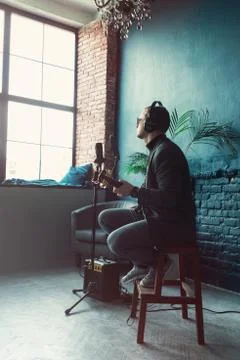 Close up of a man singer sitting on a stool in a headphones with a guitar rec Stock Photos