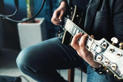 Close up of a man singer sitting on a stool in a headphones with a guitar rec Stock Photos