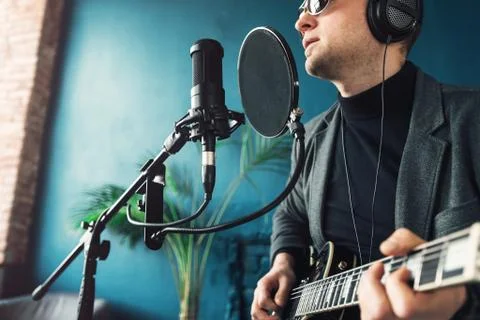 Close up of a man singer sitting on a stool in a headphones with a guitar rec Stock Photos