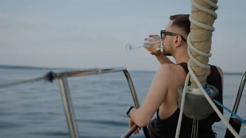 Close-up of a man sitting on the bow of a boat and drinking wine from a glass Stock Footage 201191871