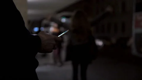 Close-up of a man sitting at a bus stop at evening using a smart phone Stock Footage 101537790