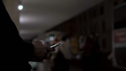 Close-up of a man sitting at a bus stop at evening using a smart phone Stock Footage 101539129