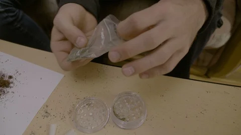Close up of a man sitting down and grinding marijuana on the table using grin Stock Footage 86877560