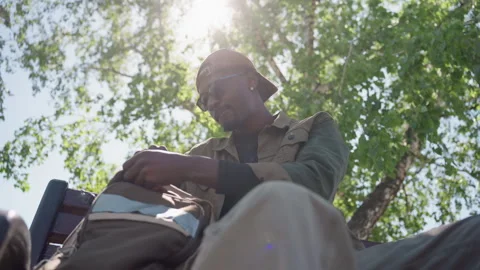 Close up of man sitting under sunlight adjusting objects on outdoor bench with Stock Footage 347970353