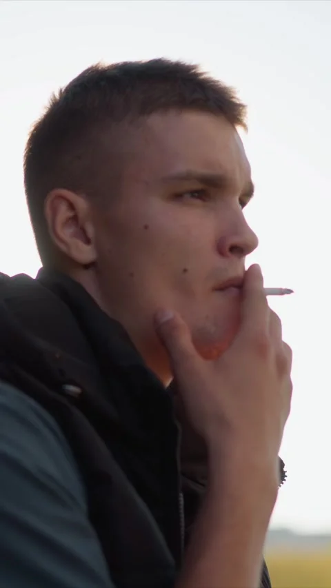 Close up of man smoking object in soft daylight with distant landscape Stock Footage 345064423
