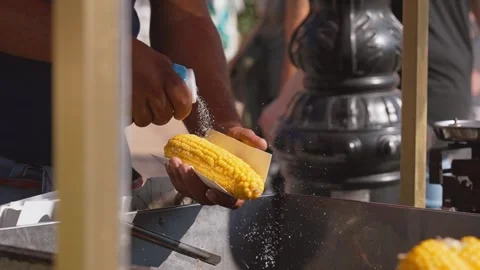 Close-up of Man Sprinkling Salt on Corn for Street Food Trading Stock Footage 258492781