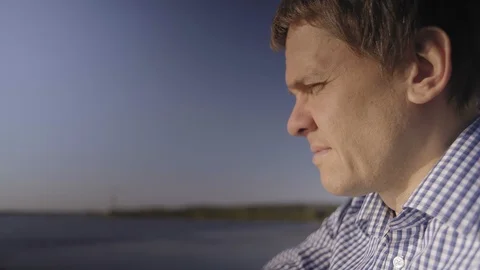 Close-up Man Squinting at the Sun and Throwing Little Pebbles into the River Stock Footage 97598248