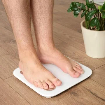Close up of man standing barefoot on digital bathroom scale measuring body we Stock Photos