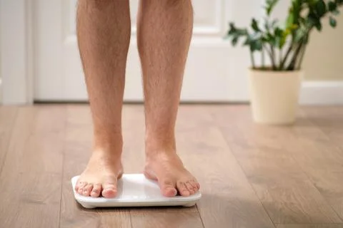 Close up of man standing on digital bathroom scale measuring body weight at h Stock Photos