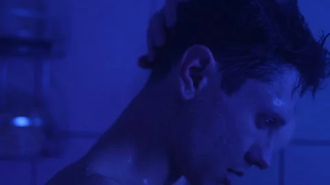 Close-up of a man standing under a shower with blue lighting, expressing deep Stock Footage 305312597