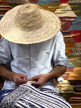 Close up man in straw hat mending carpets on sale, Essaouira, Morocco Stock Photos