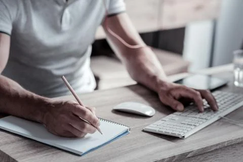 Close up of man taking notes while working on pc Stock Photos