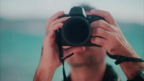 Close up of a man taking pictures with a blurry view of the sea on the Stock Footage 289854538