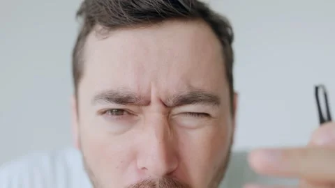Close-up of a man tweezing eyebrows, shocked reaction, self-care routine Stock Footage 306258238