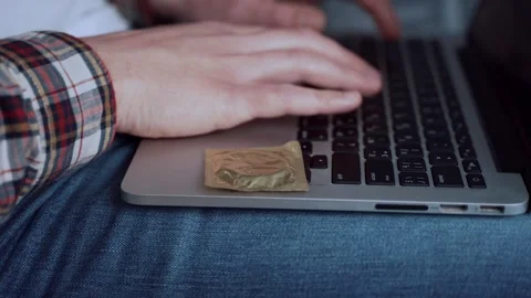 Close up of man typing on computer with a condom on the edge. Importance of Vídeo Stock 337574360