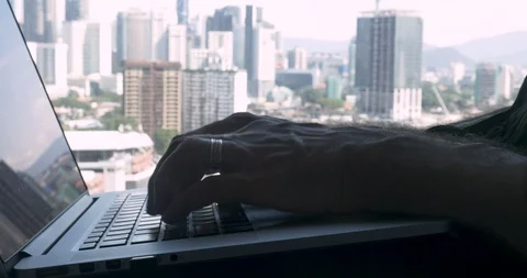 Close up of a man typing fast on a laptop computer with an office city view 스톡 동영상 86702760