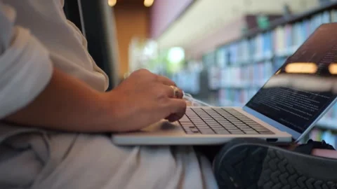 Close-up of man typing on laptop in a library. Represents focused... Stock Footage 334436948