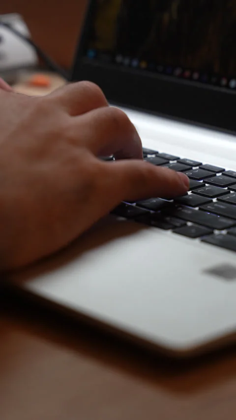 Close up of a man typing quickly on a laptop resting on a wooden desk, the Stock Footage 347743894