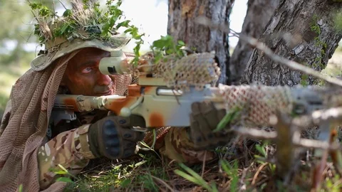 Close-up. Man in uniform looking through sniper rifle. camouflaged with grass Stock Footage 127756426