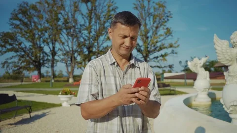 Close up man use of mobile phone walk at part near the fountain at sunlight Stock Footage 116997378