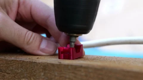 Close-up of a man using a cordless screwdriver drill to screw a red 3D printed Vídeos de archivo 345094825