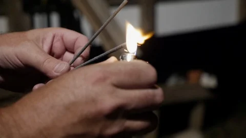 Close up of a man using a disposable lighter to ignite a sparkler at night Видео 90759269