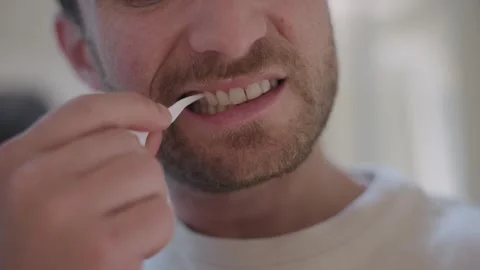 Close up of a man using a floss pick to clean his teeth, maintaining oral health 스톡 동영상 335151796