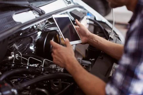 Close up of a man using his tablet to know how to fix car engine. Stock Photos