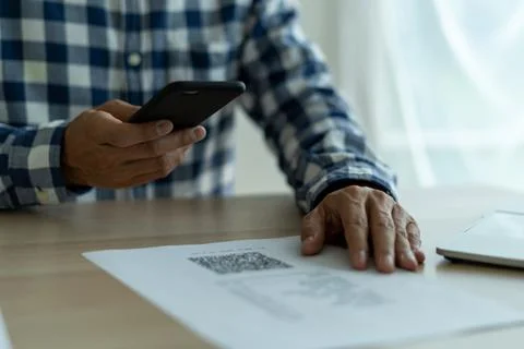 A close up of a man using a mobile smartphone to scan the QR code from an inv 스톡 사진