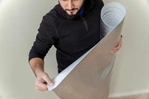 Close up of a man using a roll of insulating cloth to install a wooden floor Stock Photos