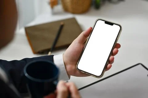 Close up man using smartphone and drinking coffee at office desk. Empty screen Stock Photos