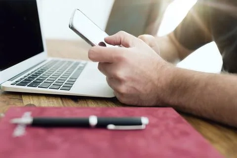 Close-up of man using smartphone in front of laptop computer in home office Stock Photos