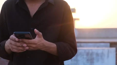 Close up of a man using a smartphone outdoors during the golden hour sunset Video stock 333451449
